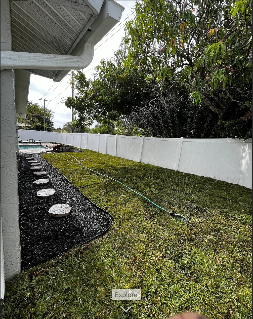 Backyard with white fence, manicured lawn, black mulch border with stepping stones, and irrigation system
