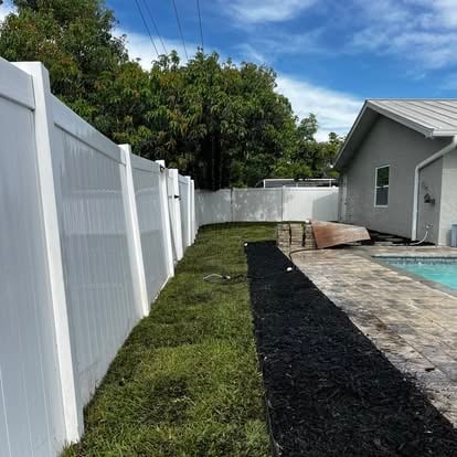 Backyard with white vinyl fence, landscaped lawn, paved patio area, and swimming pool beside a gray shed