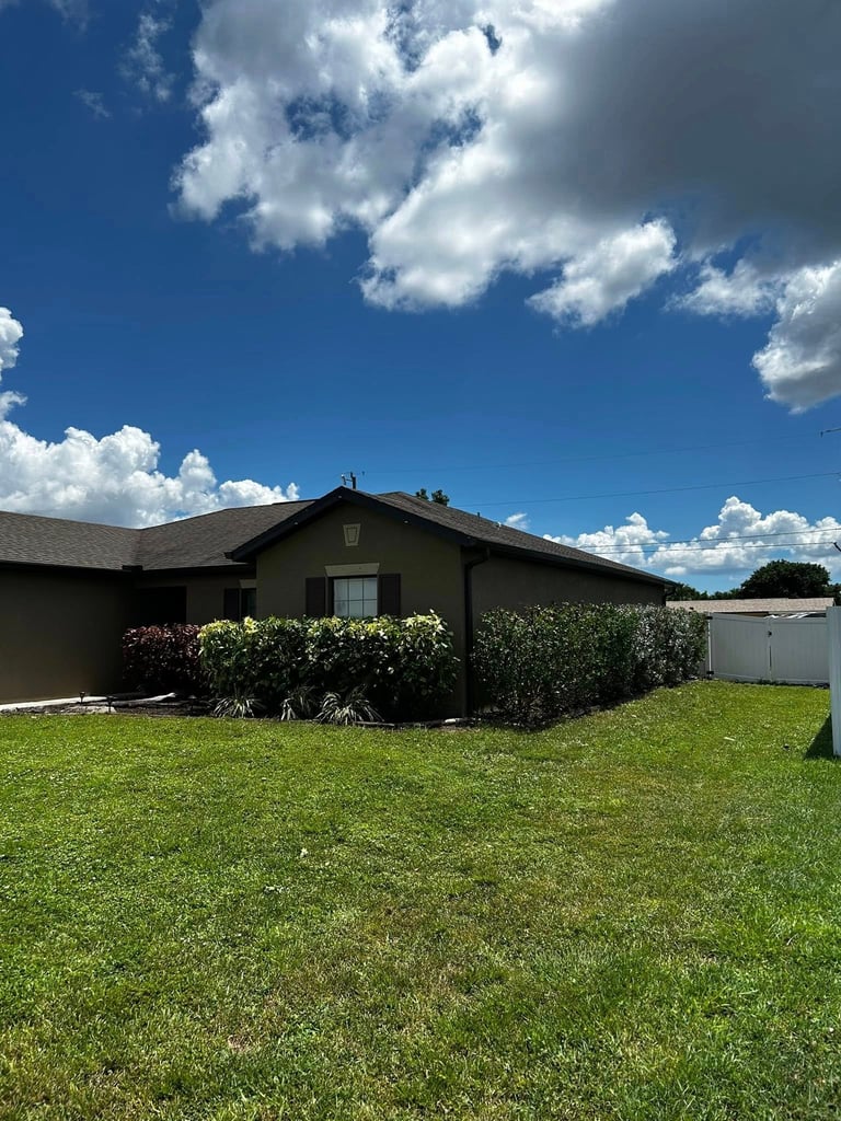 Single-story dark house with landscaping on a large green lawn under blue sky with white clouds